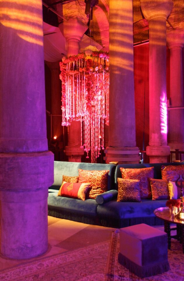 Lavishly decorated lounge with a plush sofa and mood lighting inside an event venue space with classical columns.