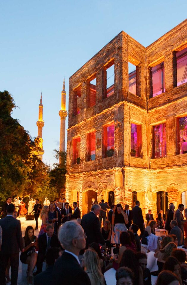 Guests gathered for an evening event outside a historic building illuminated by warm lighting with a minaret visible in the background, meticulously organized by an event planning company.