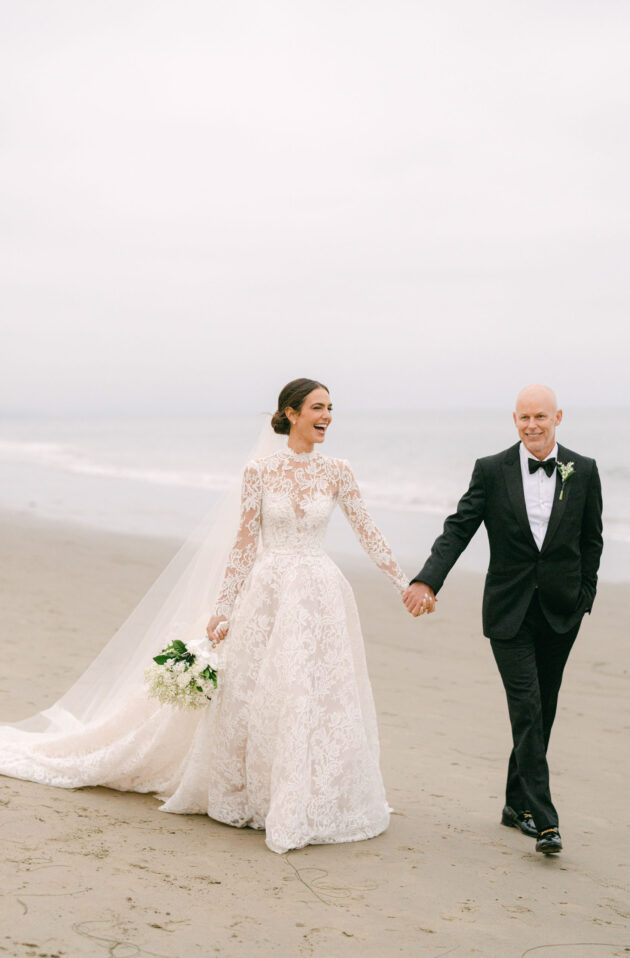 bride walking on a beach with a man in a tuxedo.
