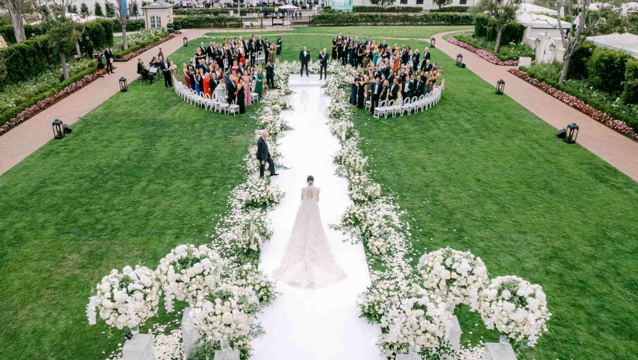 bride walking down aisle to their wedding ceremony outside on a lawn.