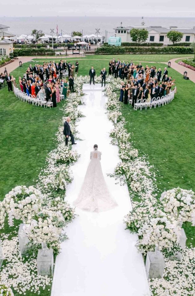 bride walking down aisle to their wedding ceremony outside on a lawn.