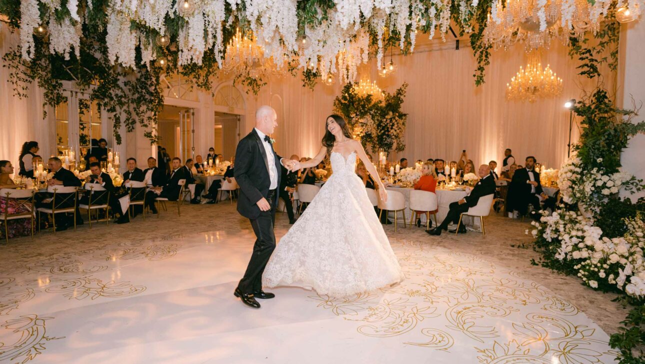 Bride and groom sharing their first dance in an elegantly decorated wedding hall, arranged by professional event planners, with guests seated around them.