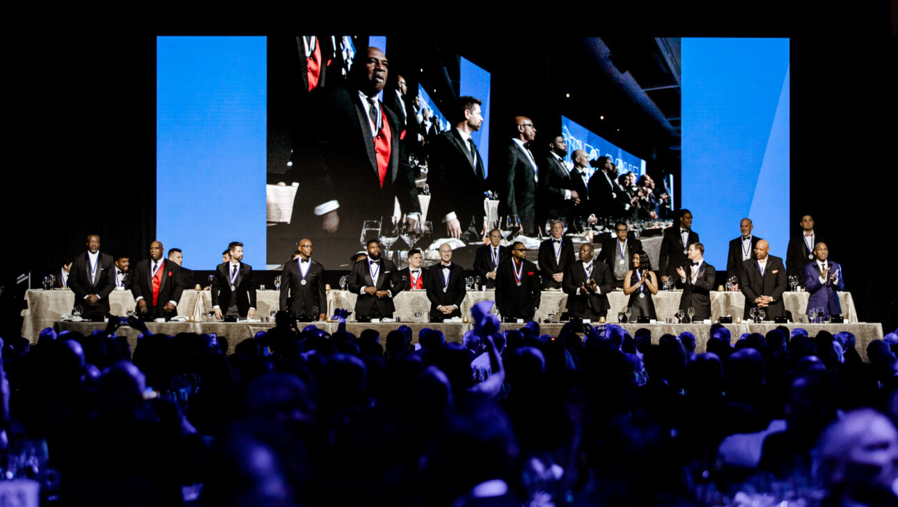 Formal dinner event with a group of people on stage being projected on large screens, organized by a top-rated event planning company.