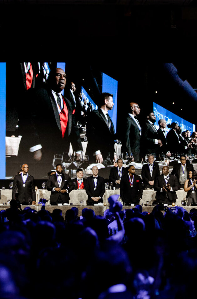 Formal dinner event with a group of people on stage being projected on large screens, organized by a top-rated event planning company.