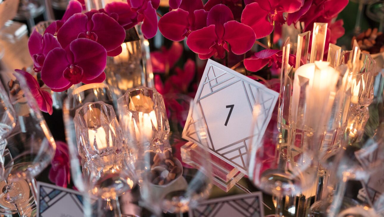 Elegant table setting at an event venue space with number 7 card, vibrant orchids, and lit candles.