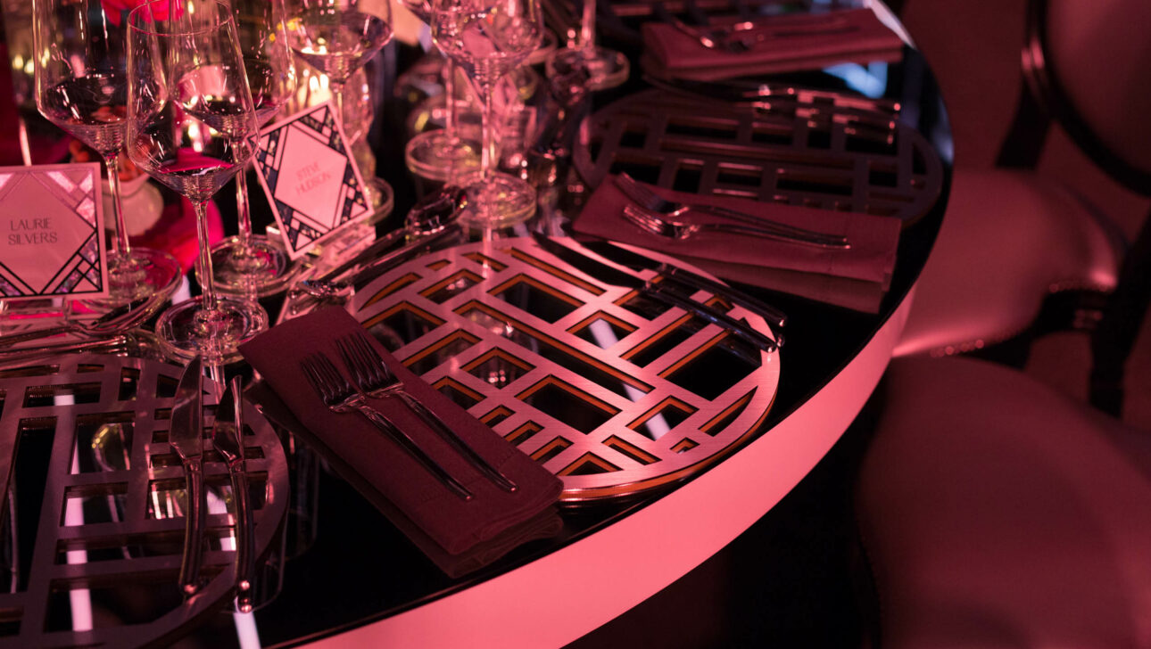 Elegant table setting with geometric charger plates and red ambient lighting at a formal event venue space.