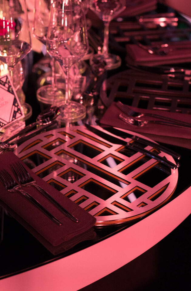 Elegant table setting with geometric charger plates and red ambient lighting at a formal event venue space.