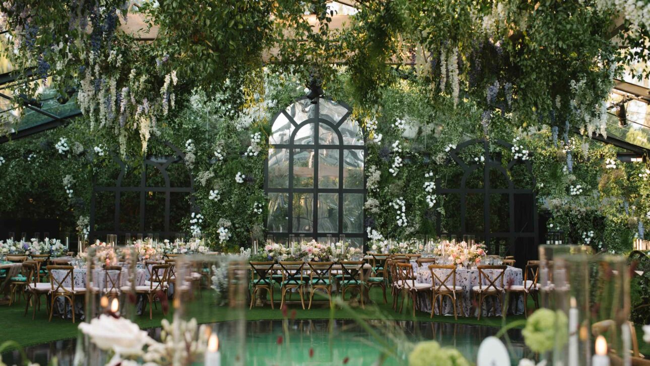 elaborate decorated dining tables under floral arrangements in a green house.