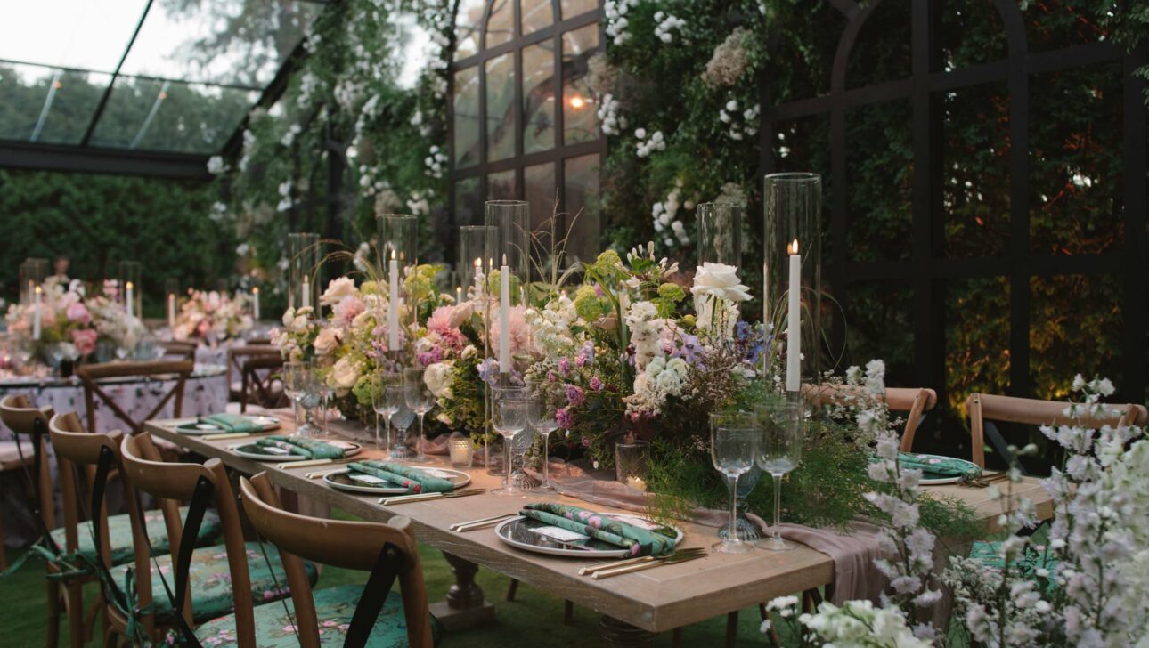 dining table decorated with flowers and place settings in a greenhouse.