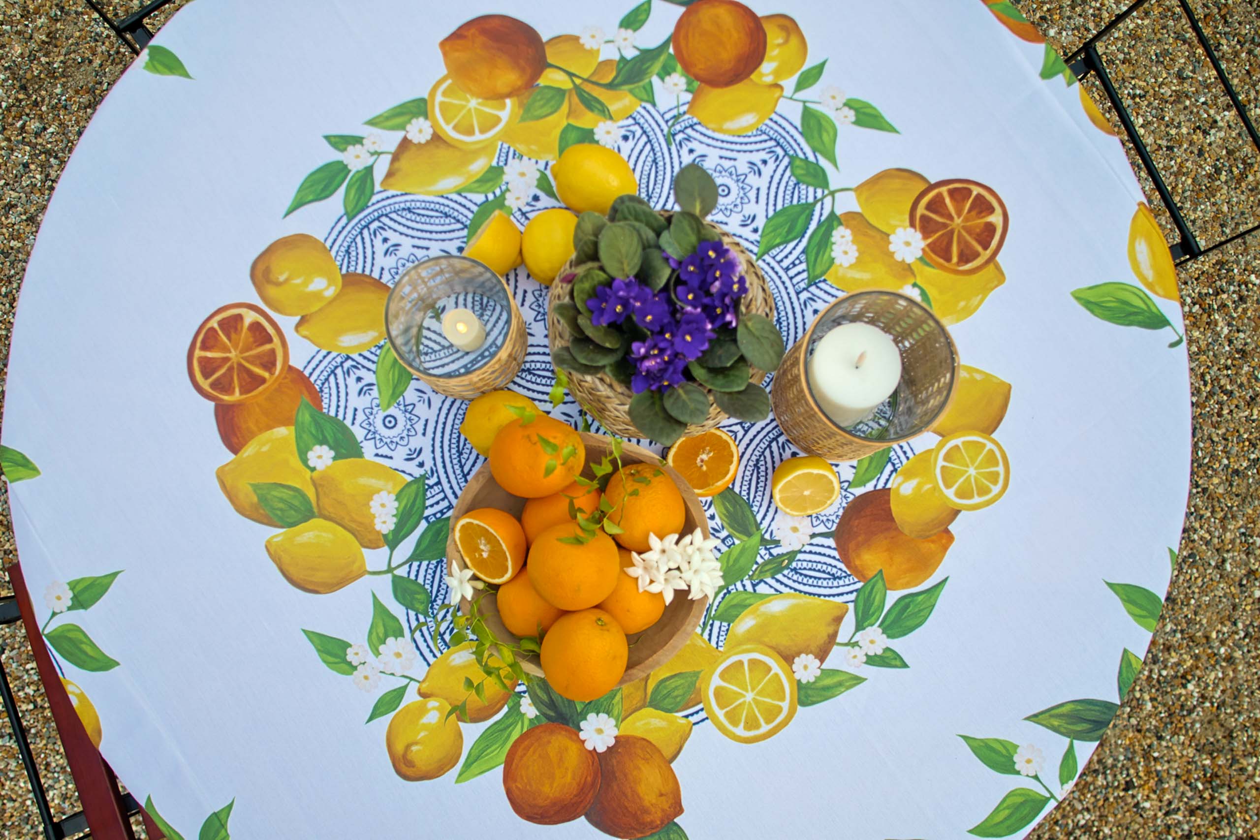 A colorful table setting prepared by our event planning company, with a lemon-themed tablecloth, featuring whole and sliced oranges, candles, and a small floral arrangement.