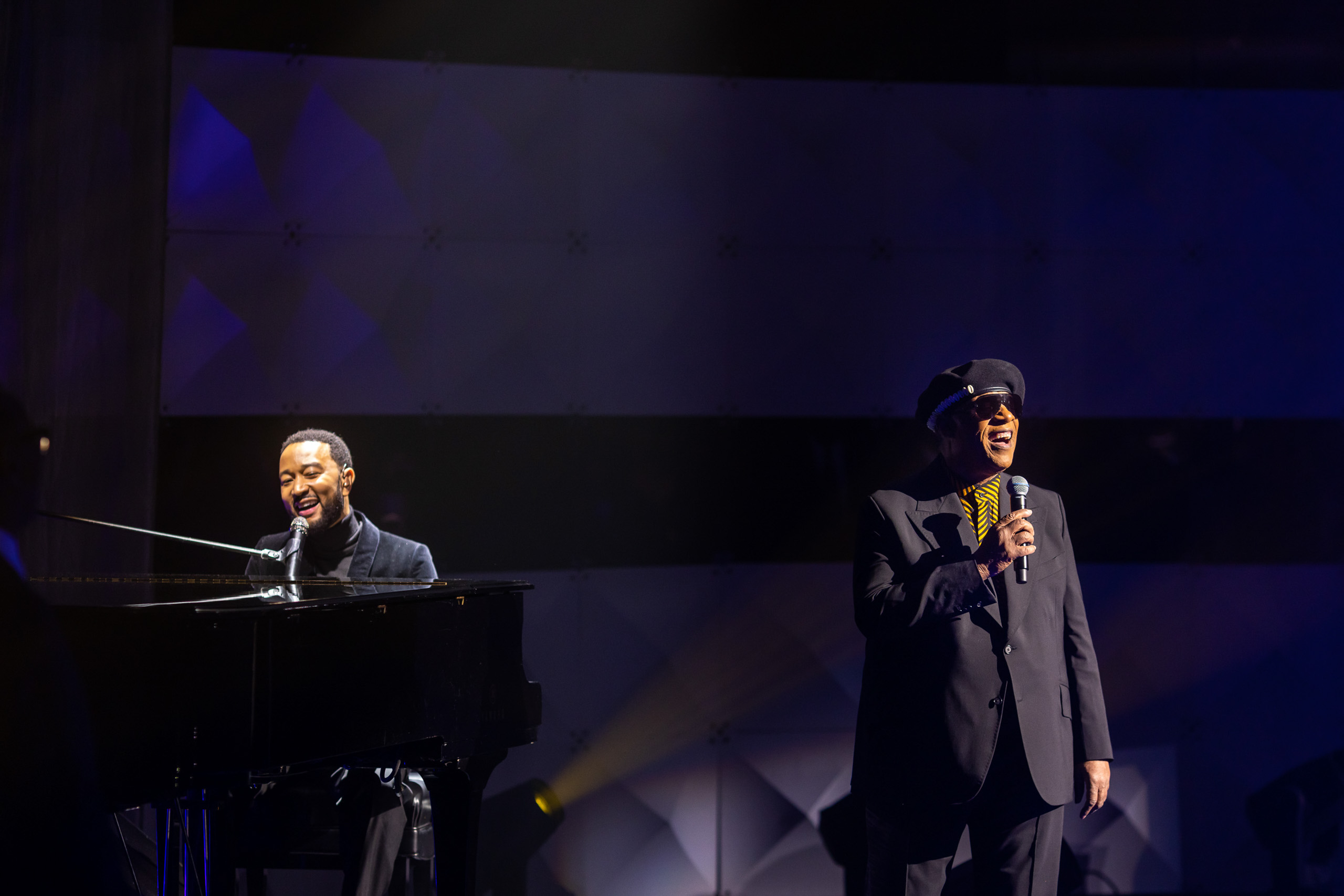 Two musicians, booked by a renowned event planning company, performing on stage; one playing the piano and the other singing into a microphone.