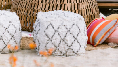 Beach lounge with poufs, throw pillows and furniture in sand on beach.